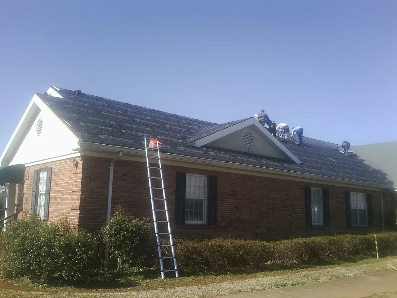 Crew tearing shingles off a brick ranch roof with a ladder set — Emergency Roof Repair work by our crew in Sewickley