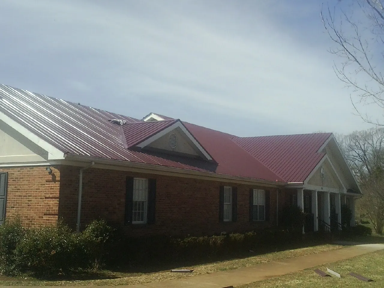 Red metal roof with gabled entries on a long brick building, from a Hail Damage Roof Repair job in Sewickley