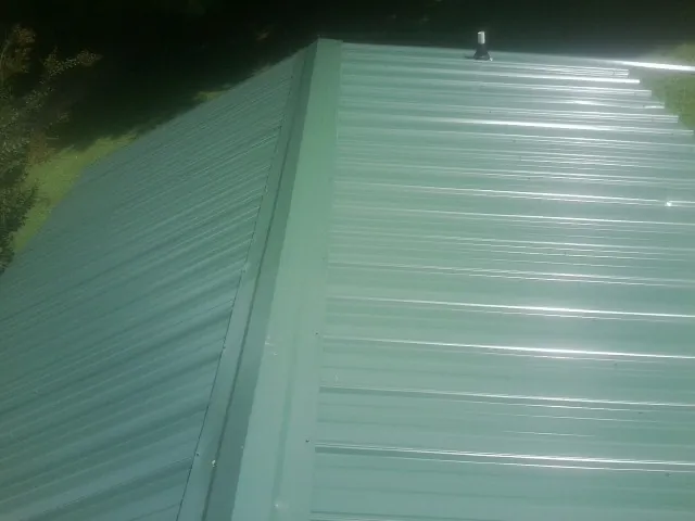 New green metal panels meeting at the ridge of a roof — Flat Roof Repair work by our crew in Sewickley