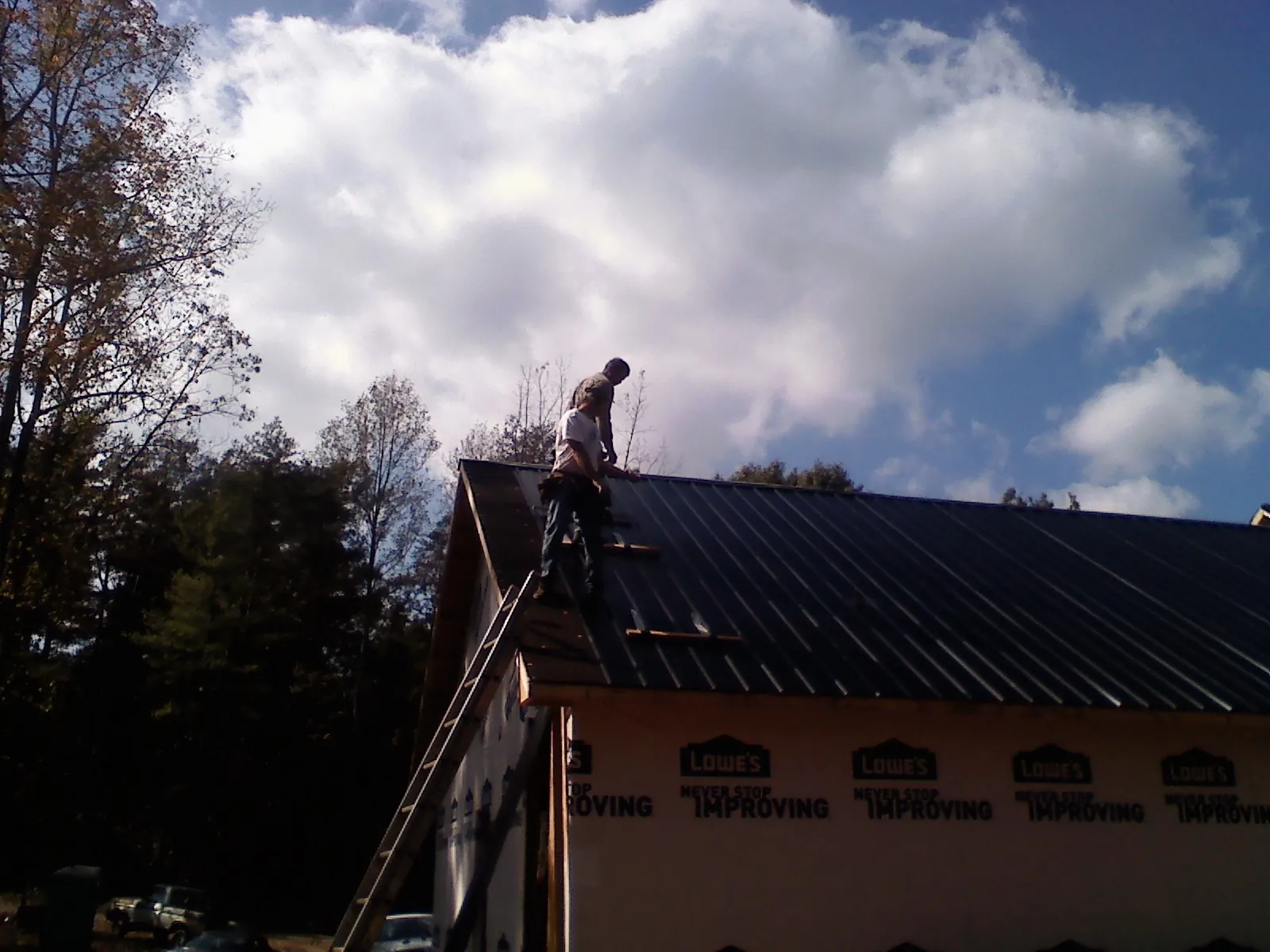 Roofer fastening dark metal panels high against a cloudy sky, from a Roof Inspection job in Sewickley