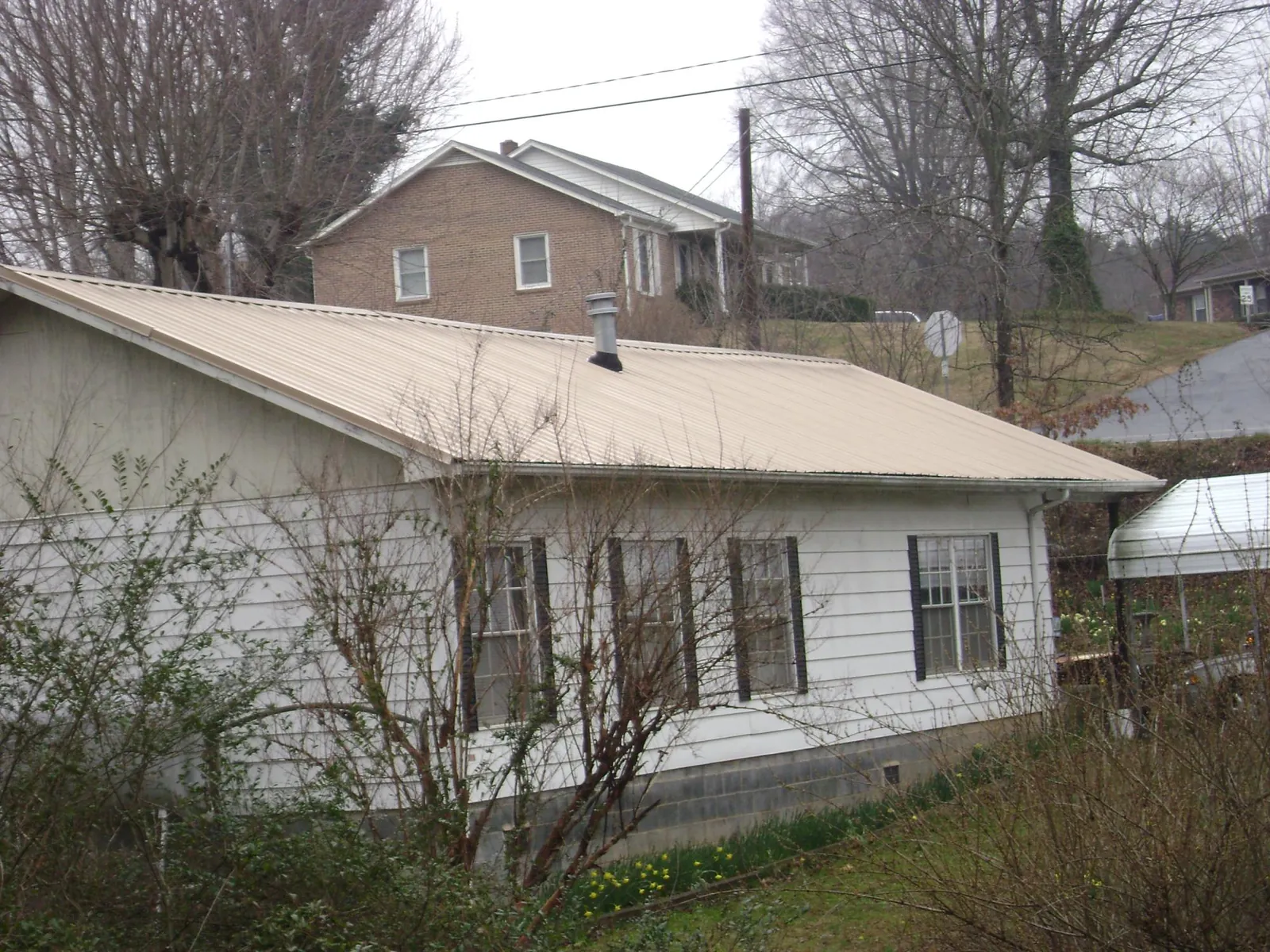 Tan metal roof on a white sided house set into a hillside — Commercial Roofing by Roofing Brothers in Sewickley
